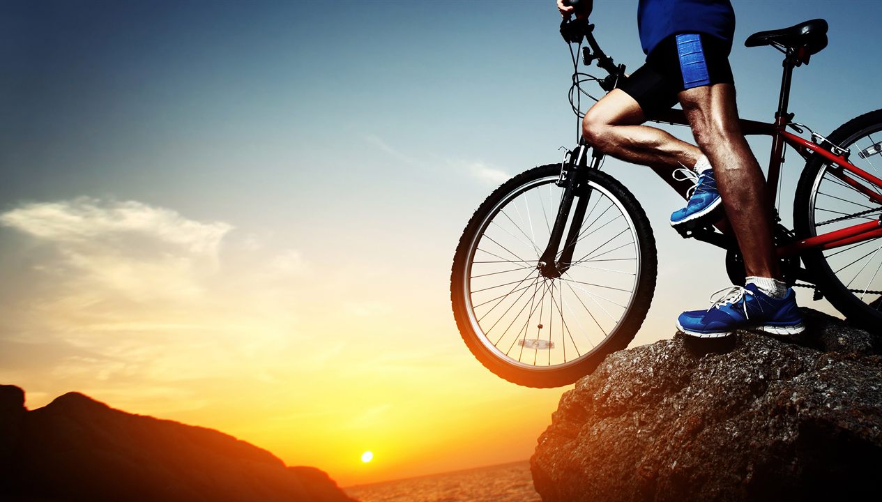 A cyclist pausing on a rocky outcrop above the sea at sunset